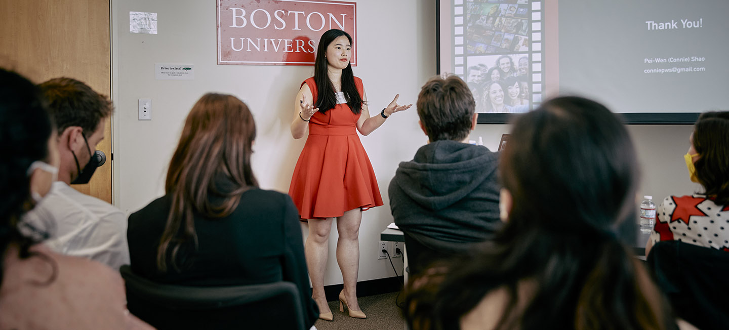 Woman in red dress speaking in front of small gathering during PitchFest 2022.
