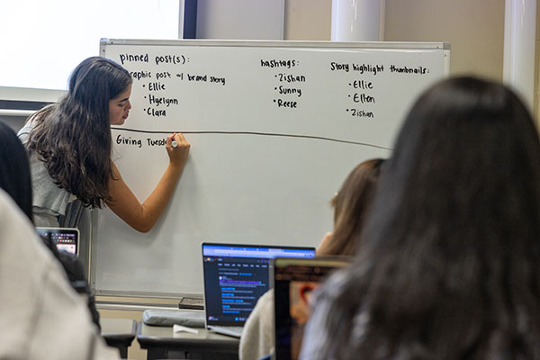 Woman writing on a white board in front of a group of people.