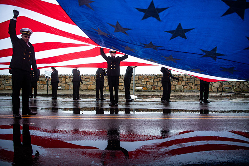 Students from Massachusetts Maritime Academy unveil a large flag during a parade.