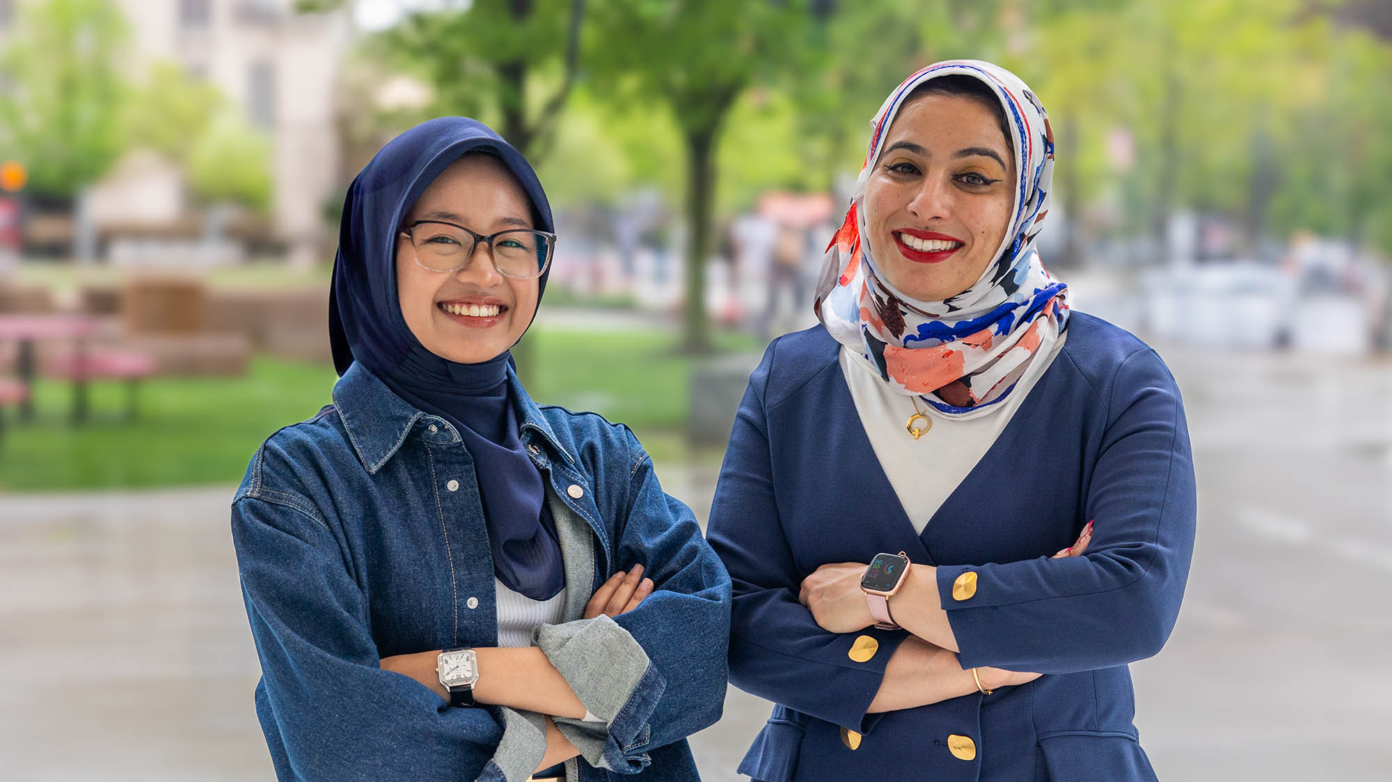 Two women, wearing head coverings, pose with their arms crossed.