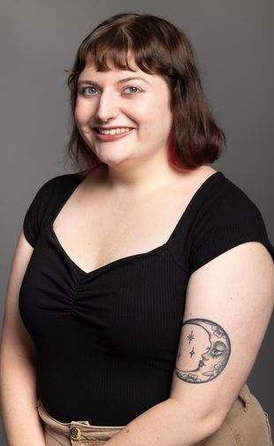 Ali with short brown hair and red highlights, smiling and posing