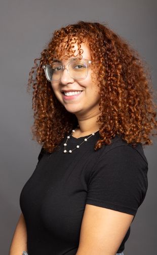 Veras, Paola with curly hair wearing a black t-shirt and glasses.