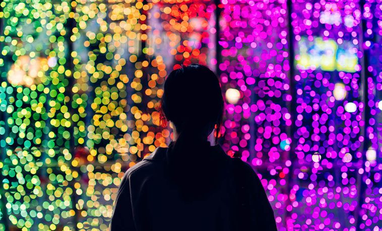 Woman in silhouette standing in front of bands of colorful lights.