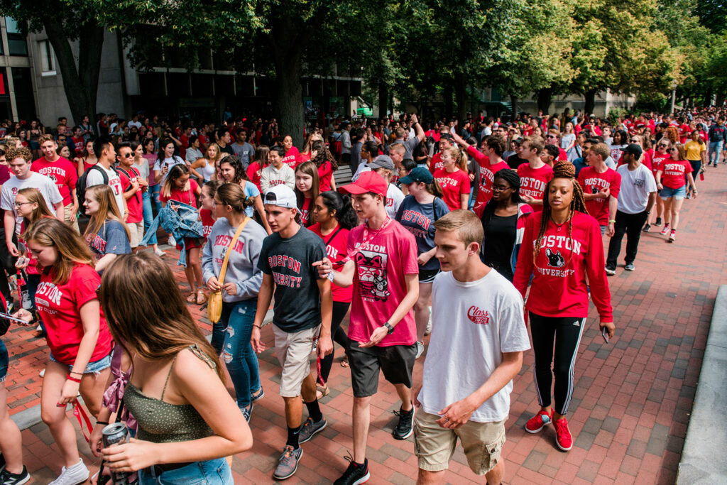 Parade of students in a variety of BU shirts walk towards Matriculation at Agganis Arena.