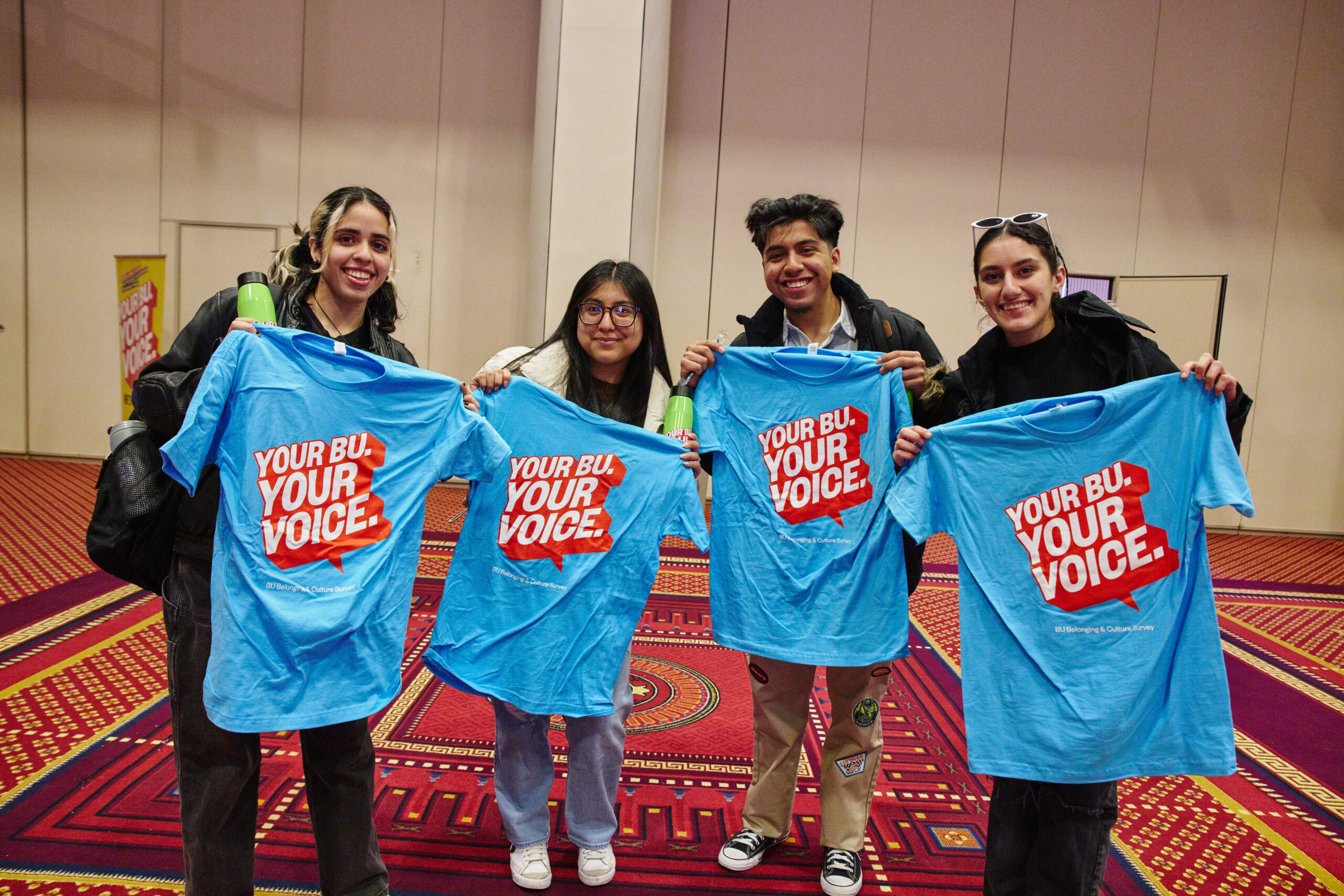 Students holding up blue t-shirts that read "Your BU. Your Voice"