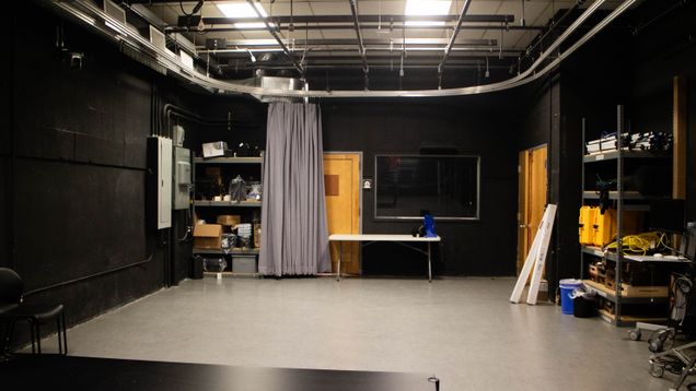 Picture of Studio 100, a blackbox space with a grey floor. It is equipped with a grey curtain for backdrops. There is no camera gear or lighting present.