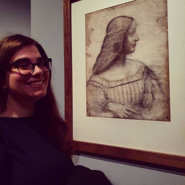 Rebecca Arnheim posing next a portrait of a woman, presumably in a museum