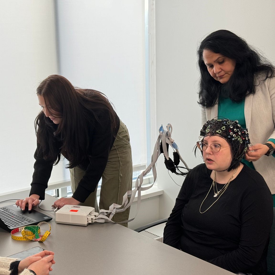 three people in a lab; one is wearing neural headgear