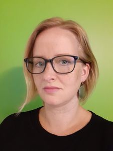 woman with short blonde hair and glasses in front of a green background