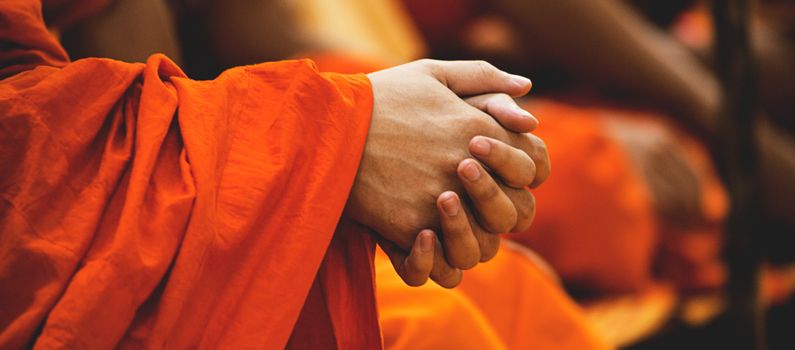 Individual in an orange robe with hands folded.