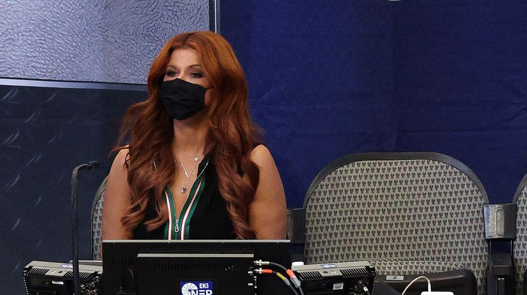Woman with long red hair wearing face mask seated behind computer