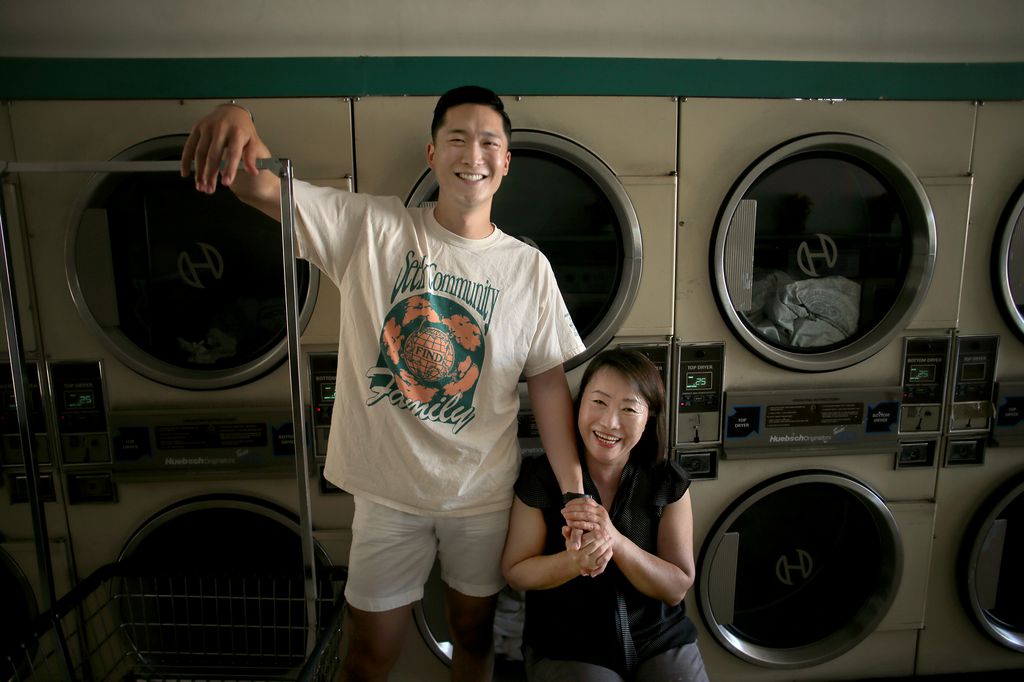 Man standing with arm around seated woman, both smile