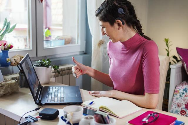 Woman with Cochlear implant gestures thumbs-up to a laptop camera