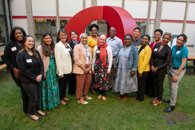 Group photo of fifteen people smiling in front of a red public art sculpture on grass