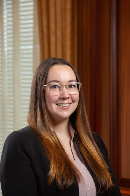Photo of Megan Segoshi. They are wearing glasses, a dark blazer, and a pink shirt. 