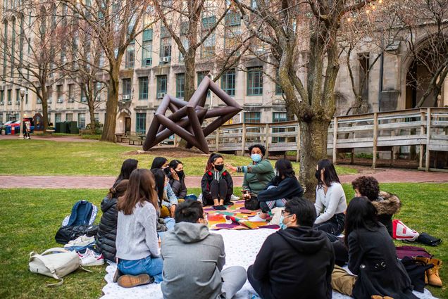 Group of students seated in a circle outdoors on a blanket listening to an instructor