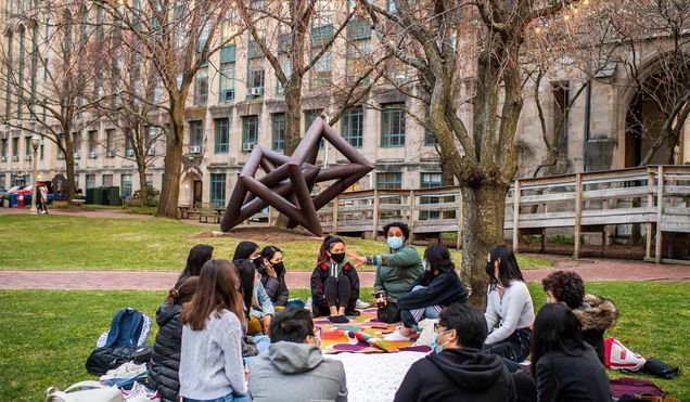 Group of students seated in a circle outdoors on a blanket listening to an instructor
