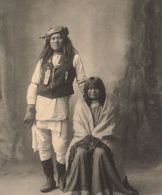 Two Native American individuals, one standing and one sitting