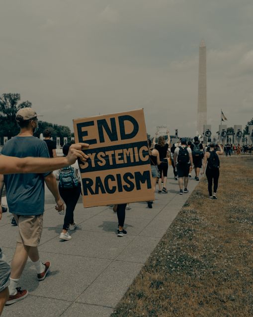 Person holding a sign stating End Systemic Racism in front of the U.S. Washington Monument
