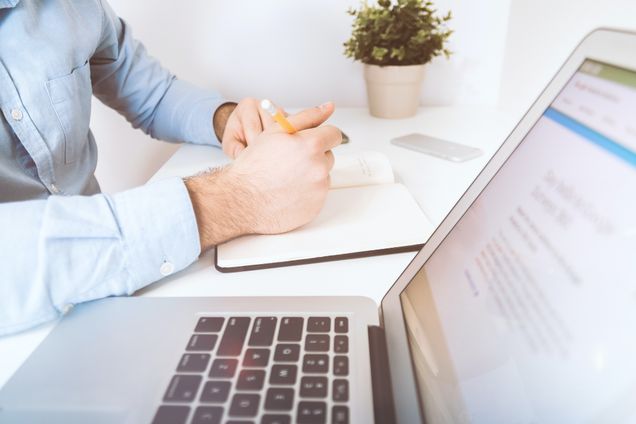 Man writing in a notebook next to laptop