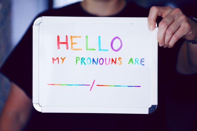 Person holding whiteboard with words "Hello my pronouns are __/__"