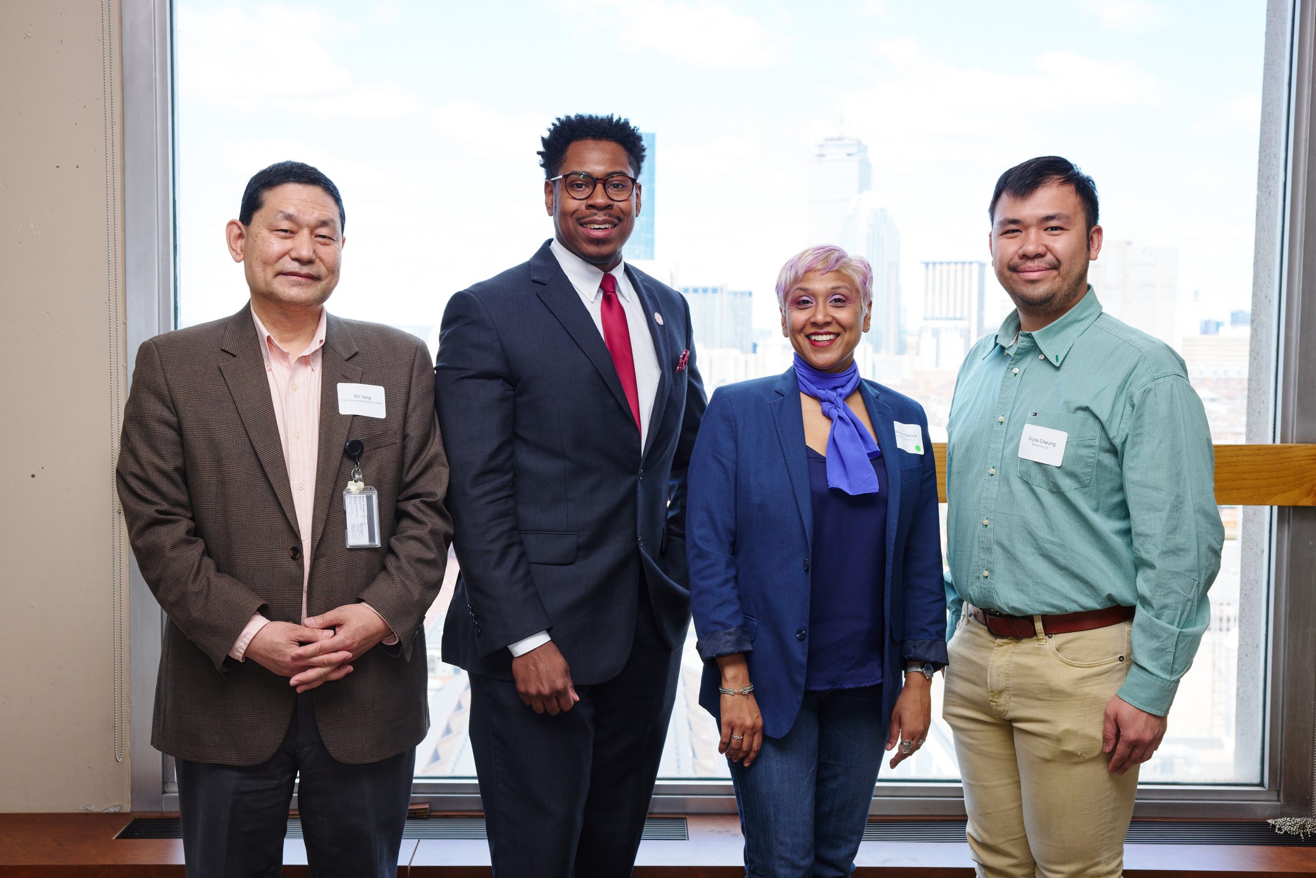 Four people stand shoulder to shoulder and smiling