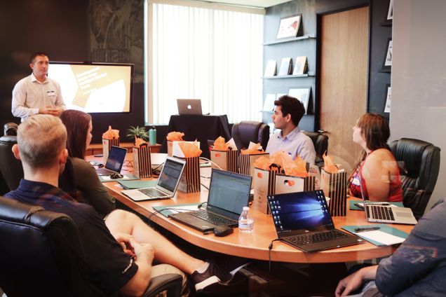 Conference table with four workers and a person giving a presentation