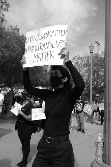 Protestors protesting for Black Lives Matter, person holding sign stating "#BlackLivesMatter #BlackTransLivesMatter"