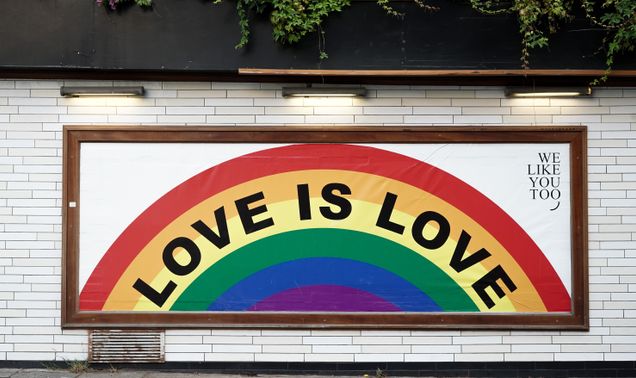 Mural on white brick wall with a rainbow with the words Love is Love and We Like You Too