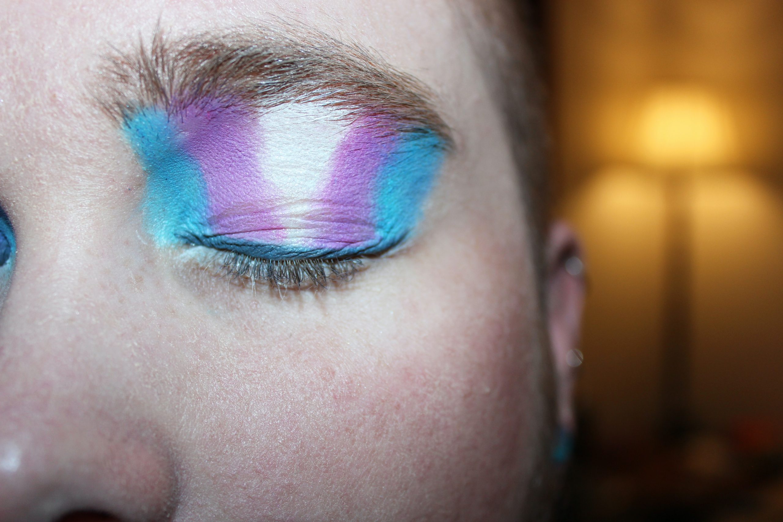 A person's eye with the transgender flag on the eyelid