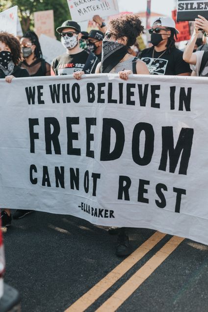 People at protests holding signs, with a banner stating: We who believe in freedom cannot rest Ella Baker