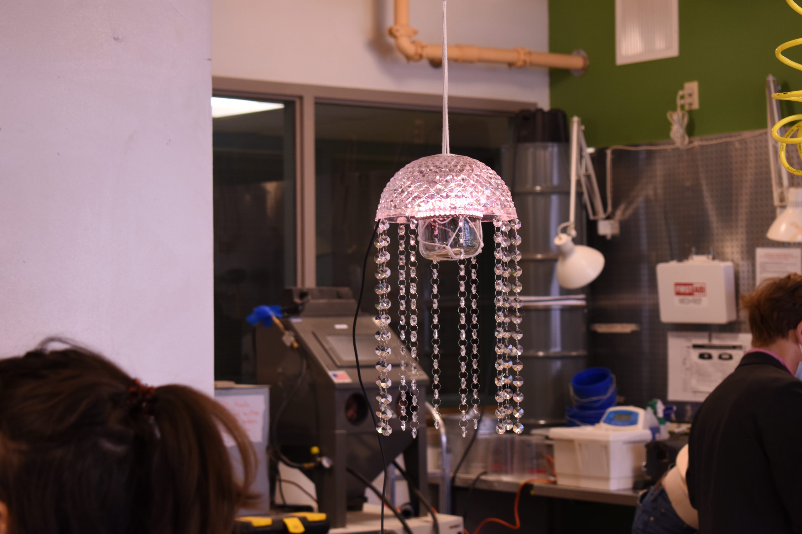 an upside down textured clear glass bowl with glass bead strings hanging down from the edges, there is a clear glass jar suspended in the middle of the bowl hiding the light and wires