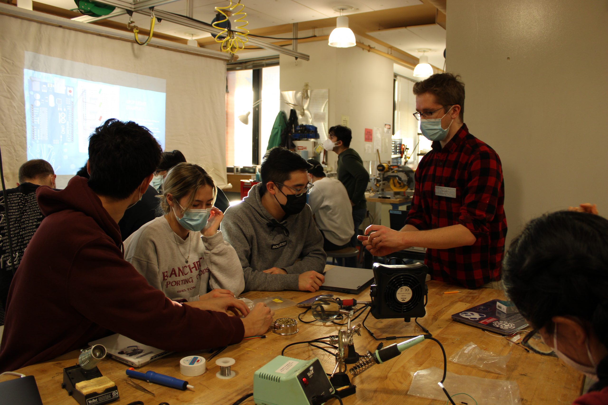 A close shot of one of the tables from the Lutron Lighting Arduino and Soldering workshop with 1 person showing the others what a good soldering connection will look like
