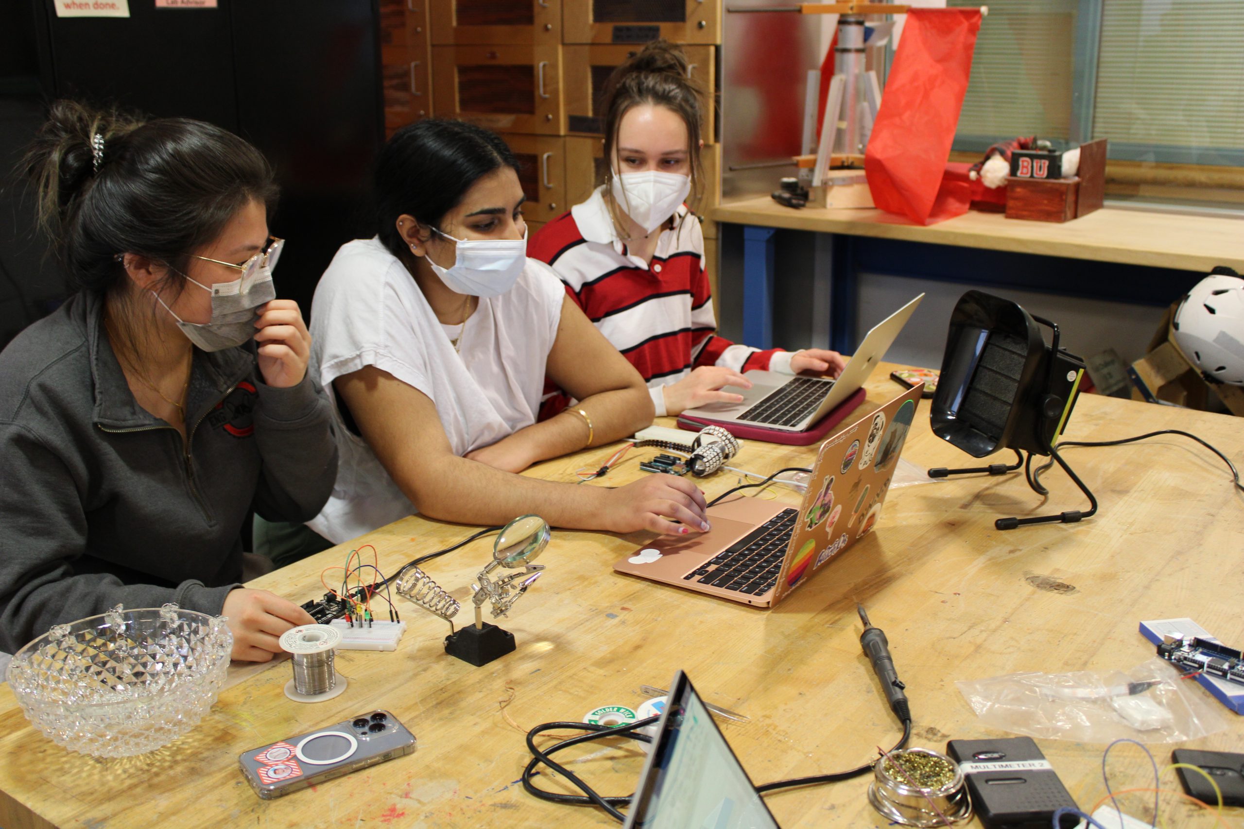 a close up of one table from the Lutron Lighting Ardiuno and Soldering workshop, a group of 3 students clustered around 2 laptops