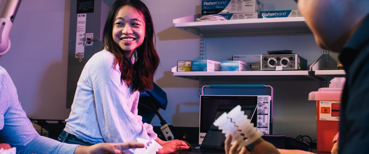 Female engineering student smiling as she works with other students in a lab setting