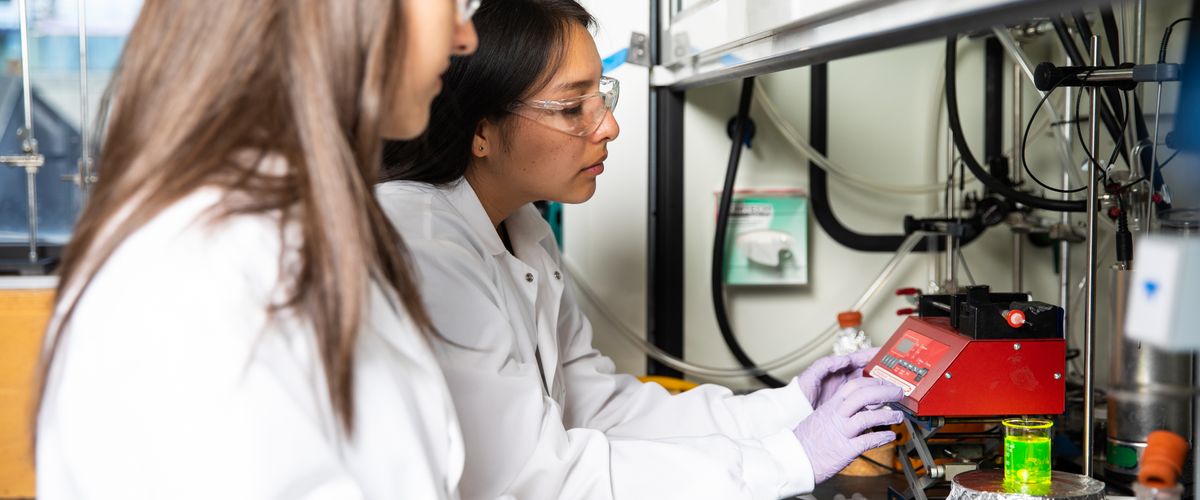 Two College of Engineering students wearing safety glasses while working with polymeric nanoparticles