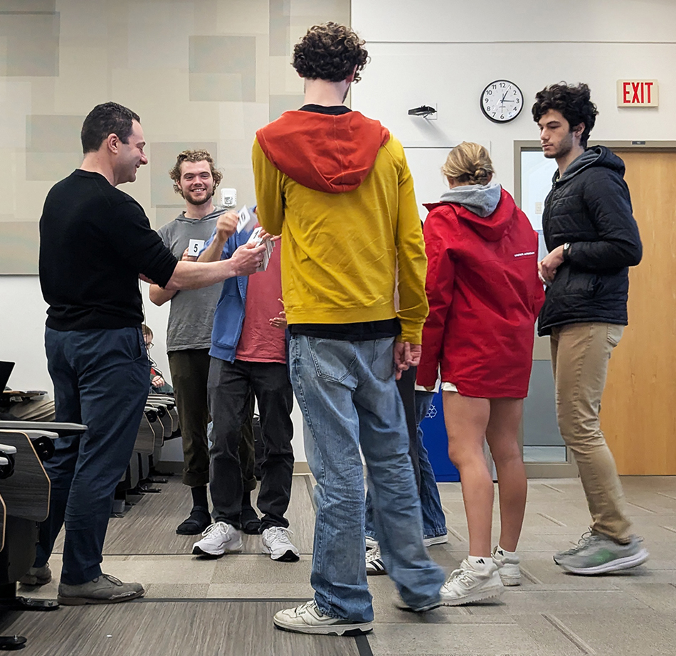 Professor Ed Solovey stands with a group of BU undergrads, to whom he is handing out small cards.