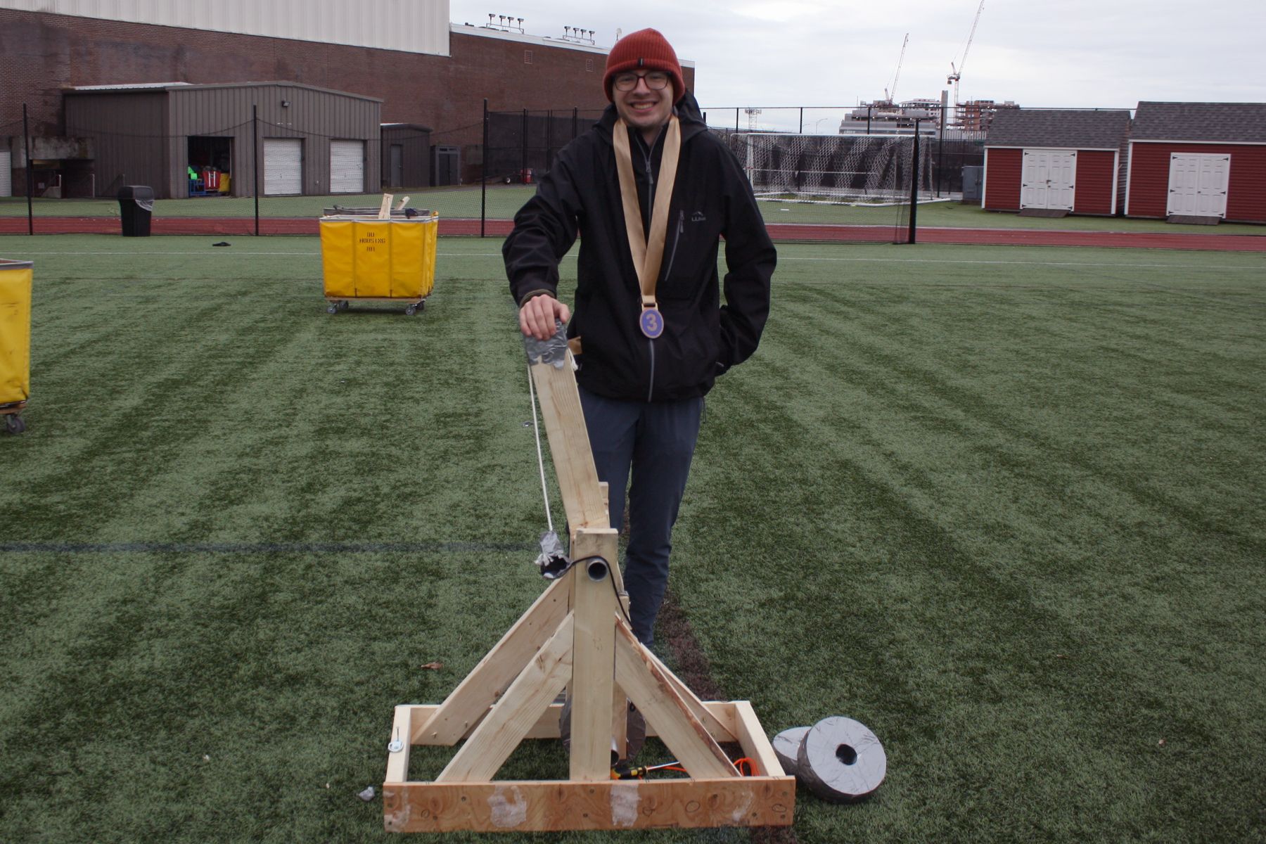 a student stands next to his catapult with a bronze ribbon around his neck