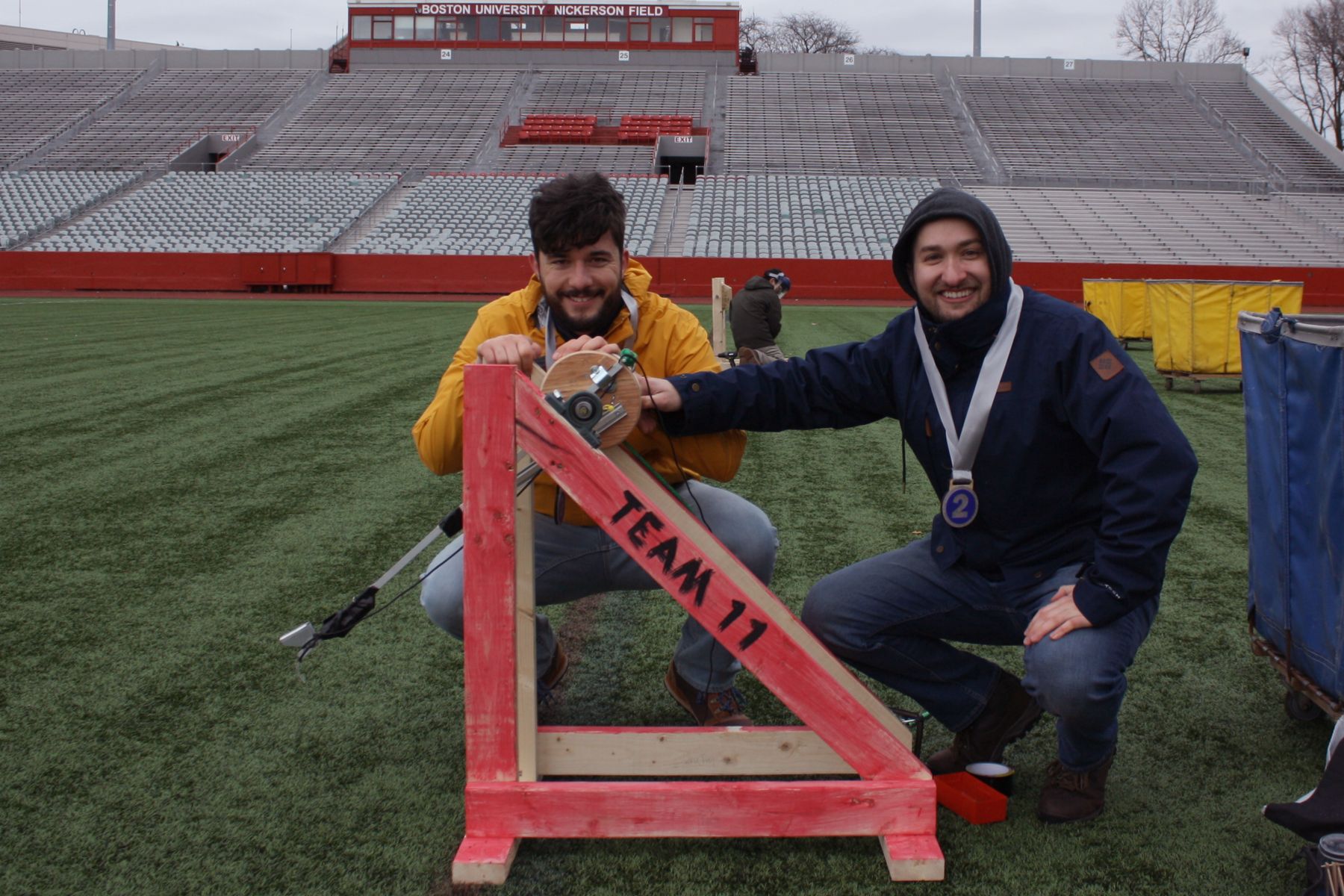 2 students crouch next to their catapult with second place ribbons around their necks