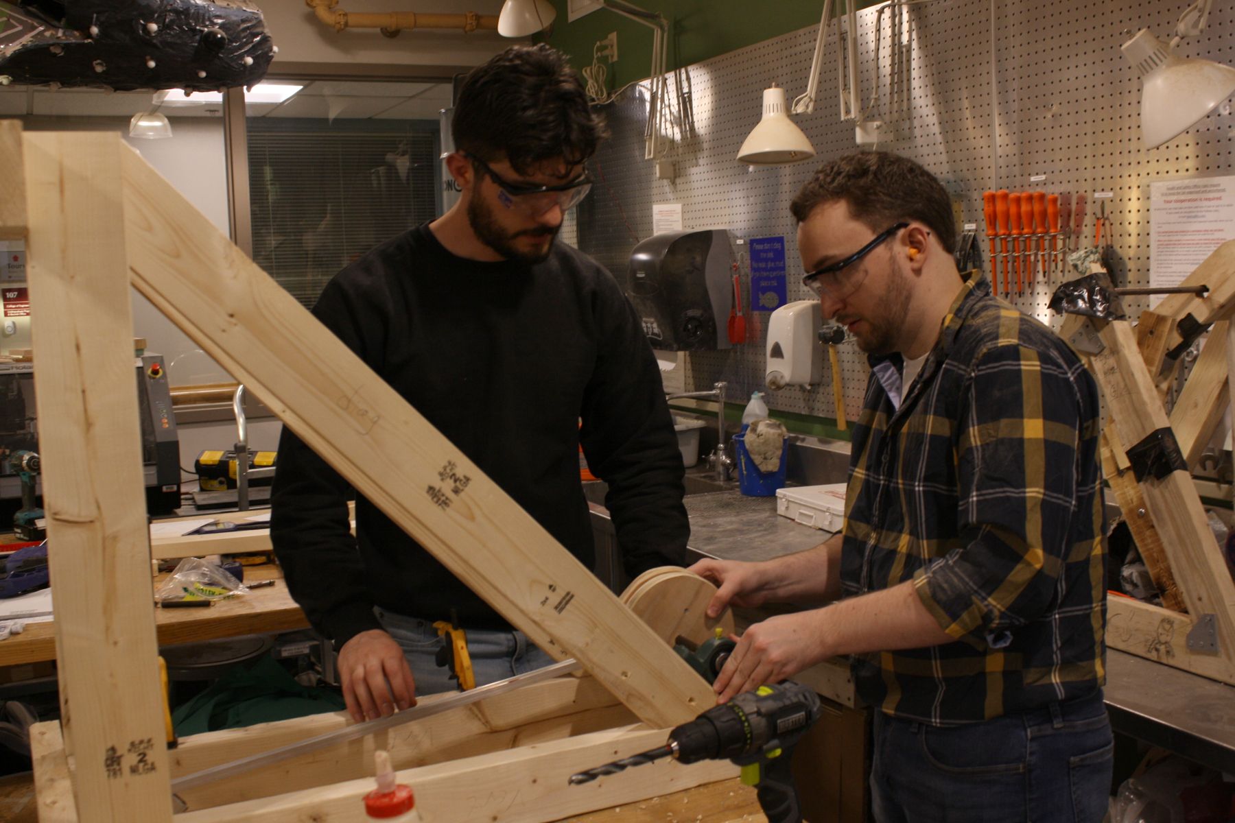 2 students stand at a partially assembled catapult, holding the launch stick to figure out where to put it