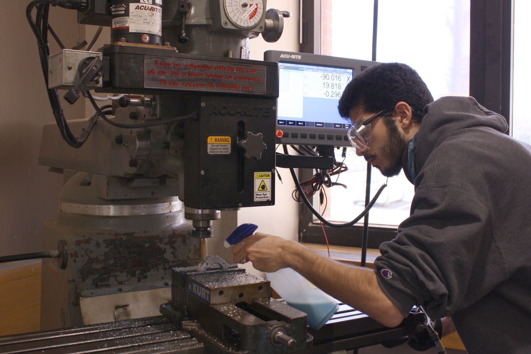 a student spraying coolant on the bit while he uses the NC mill to cut into a block of aluminum