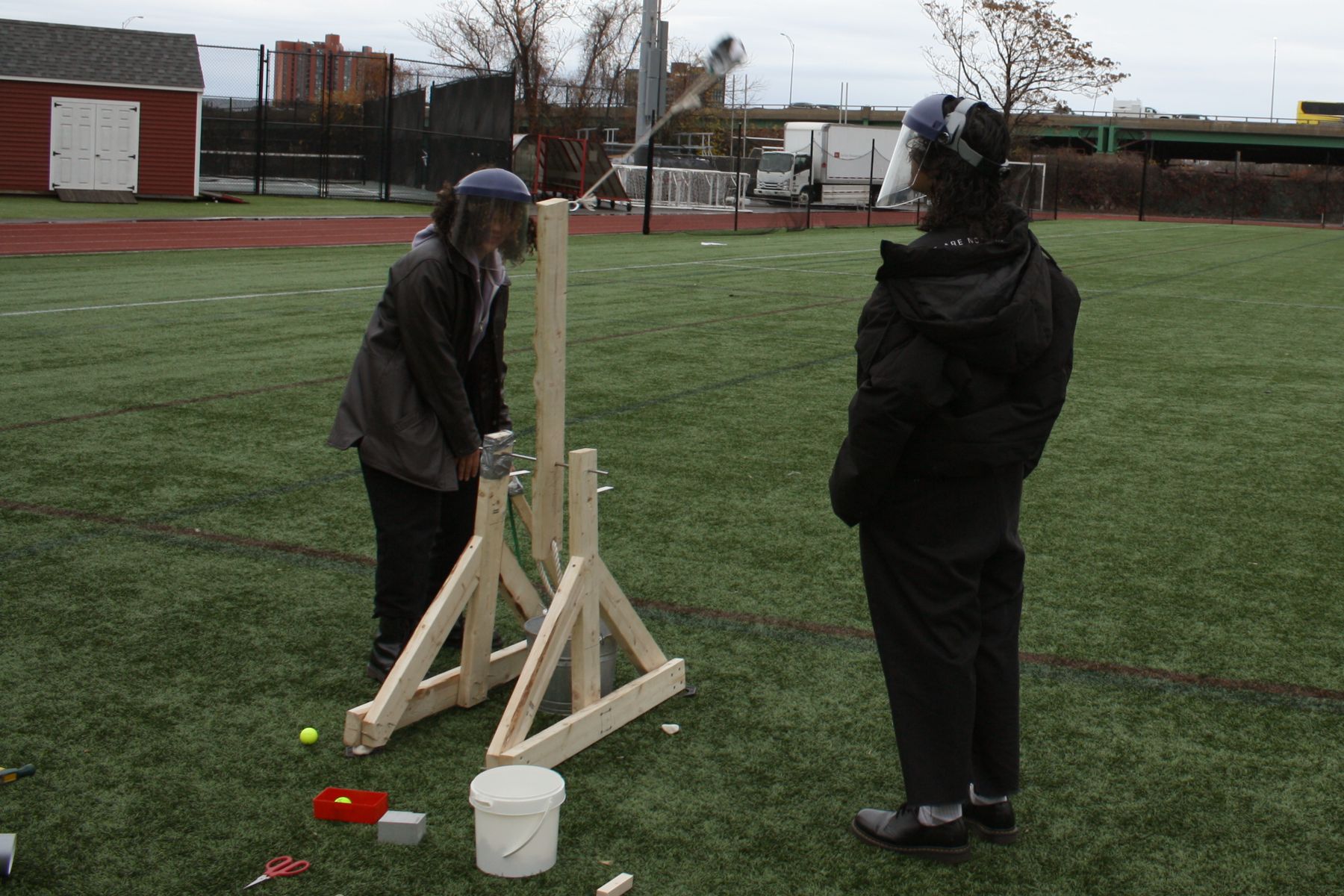 2 students stand next to their catapult as it launches