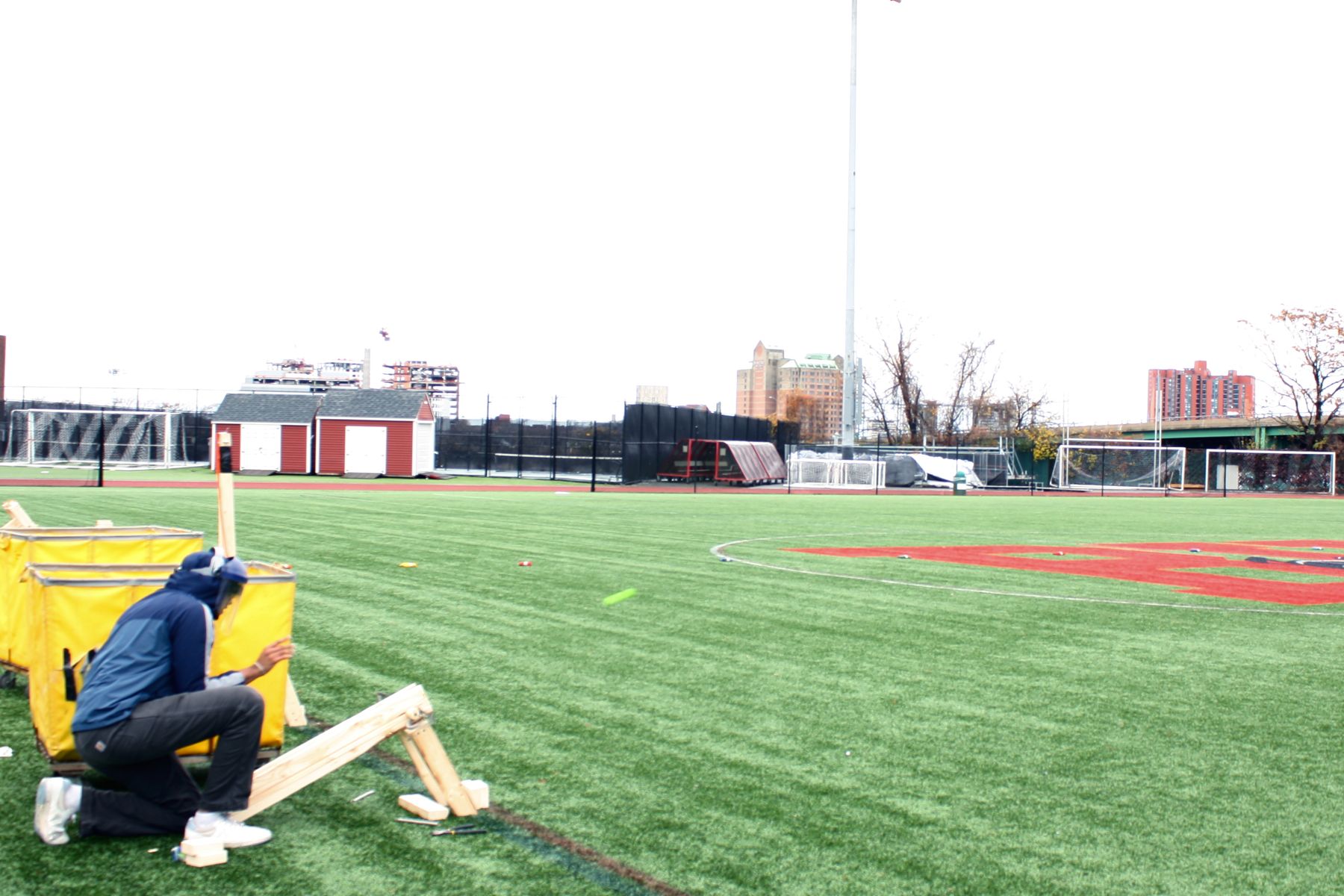 a student crouches next to hsi catapult as it launches, you can see a bright green smudge of the golf ball in motion near the catapult