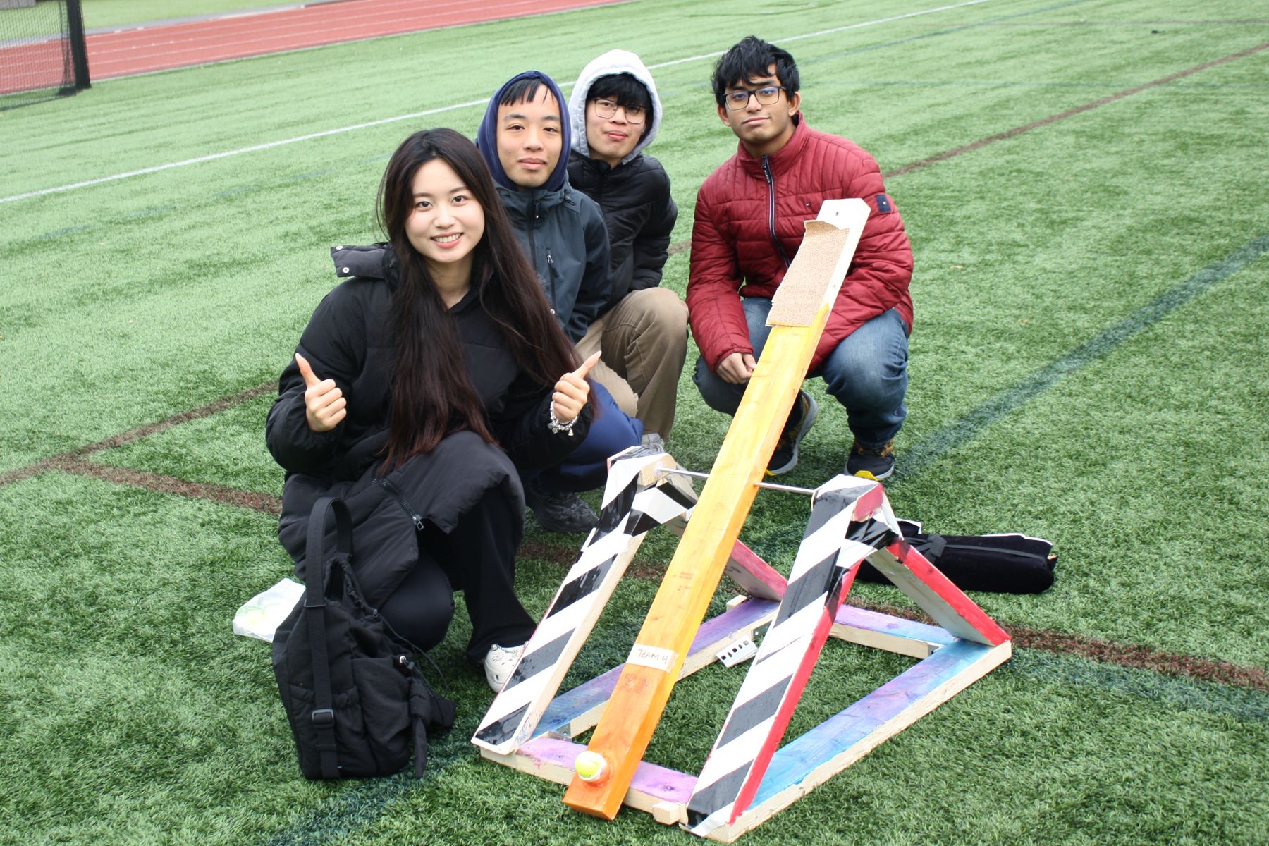 4 students crouch smiling next to their catapult