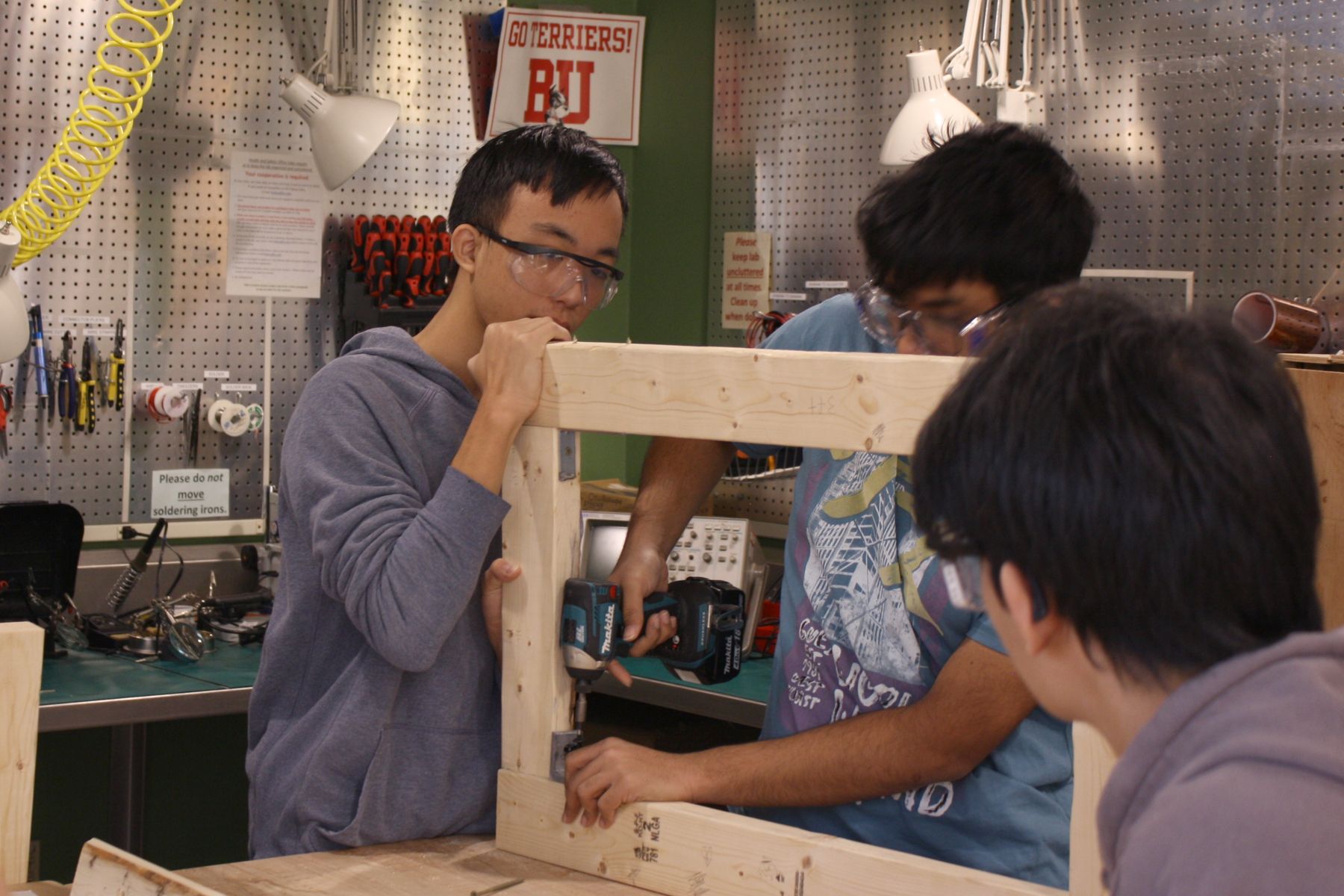 3 students holding and drilling together a frame for their catapult