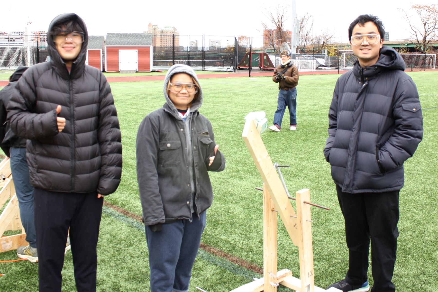 3 students stand smiling next to their catapult