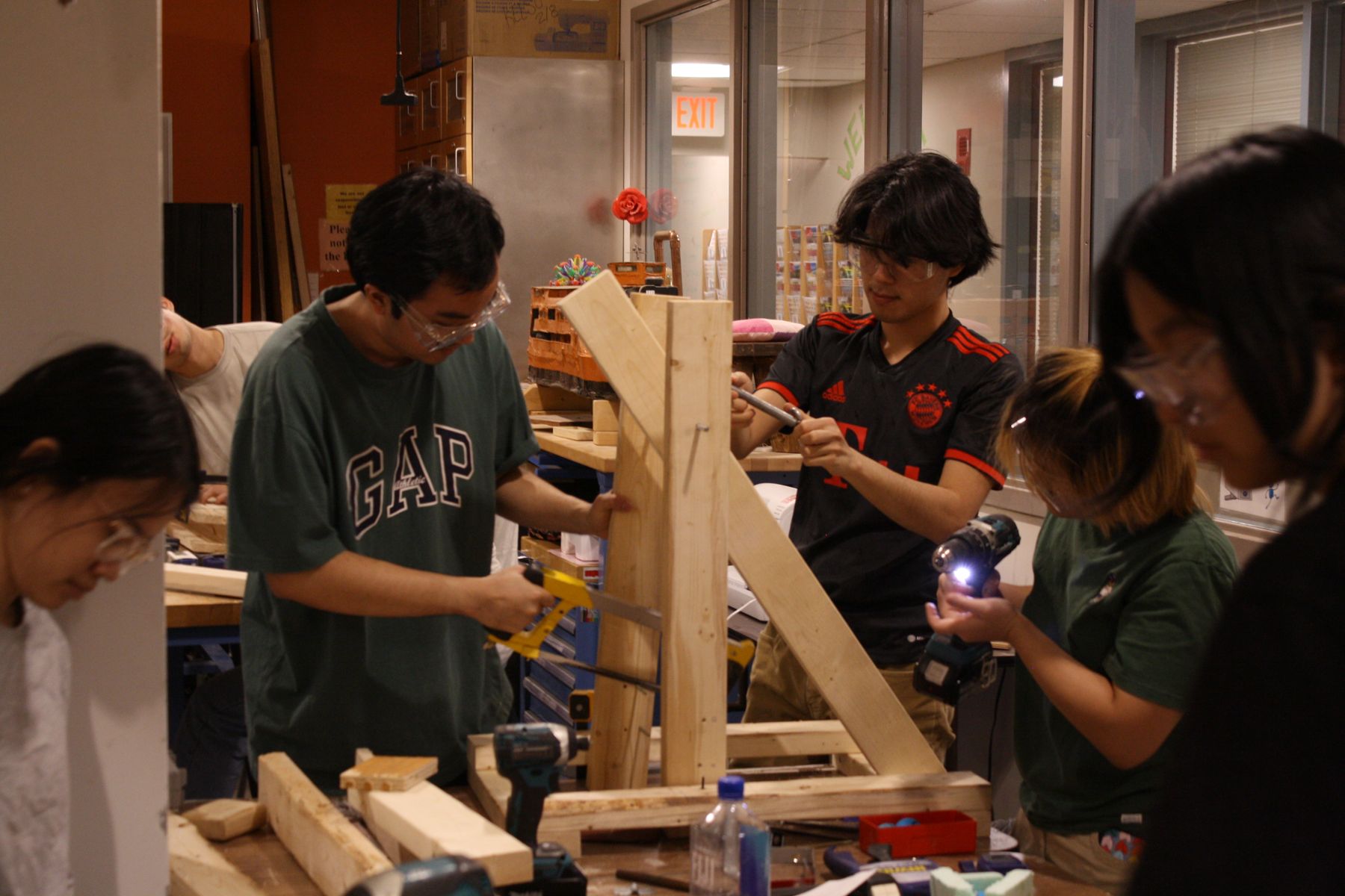 3 students in the midground work in various ways on their catapult