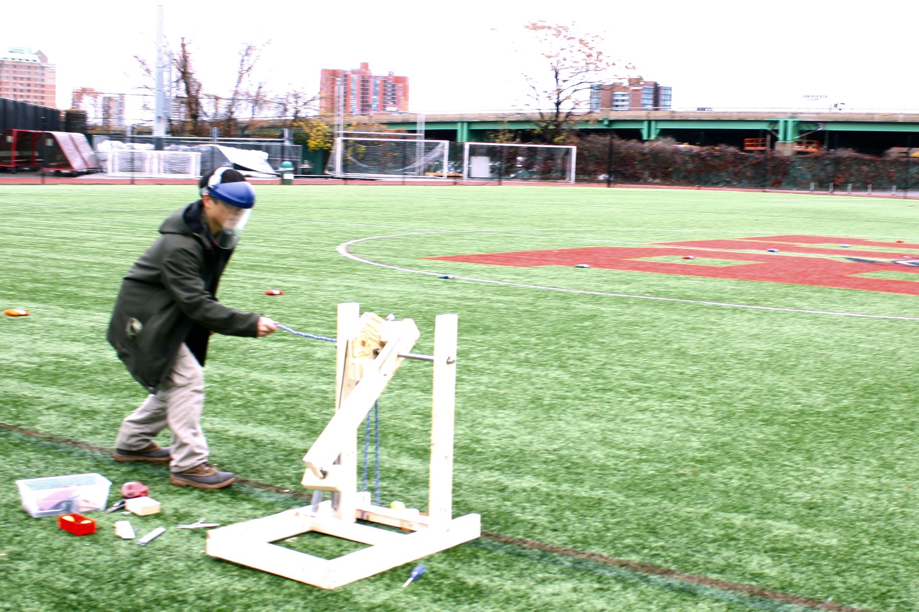 a student crouches next to his catapult as he pulls the cord to launch the golf ball