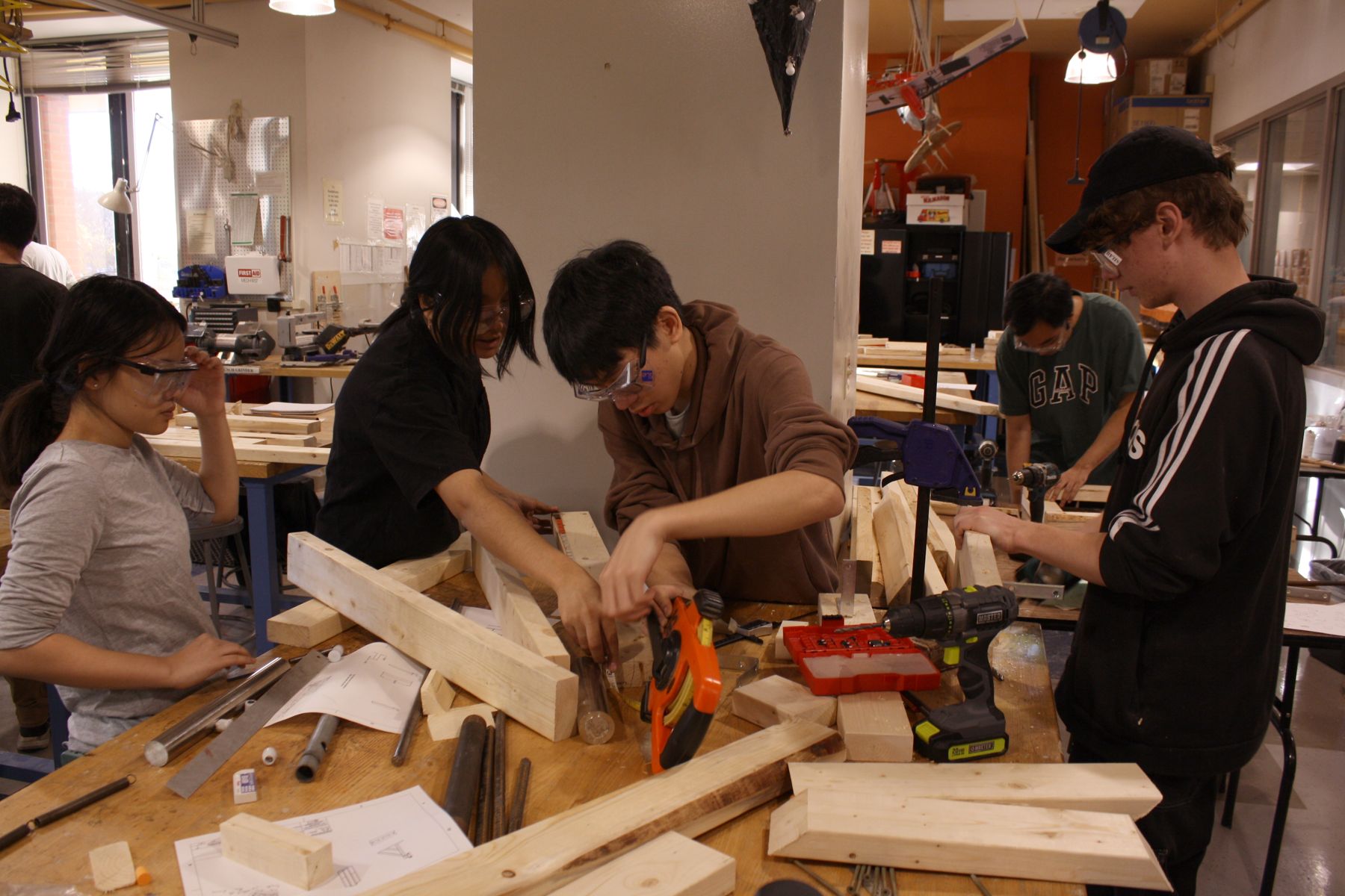 4 students working at a table full of wood and other materials