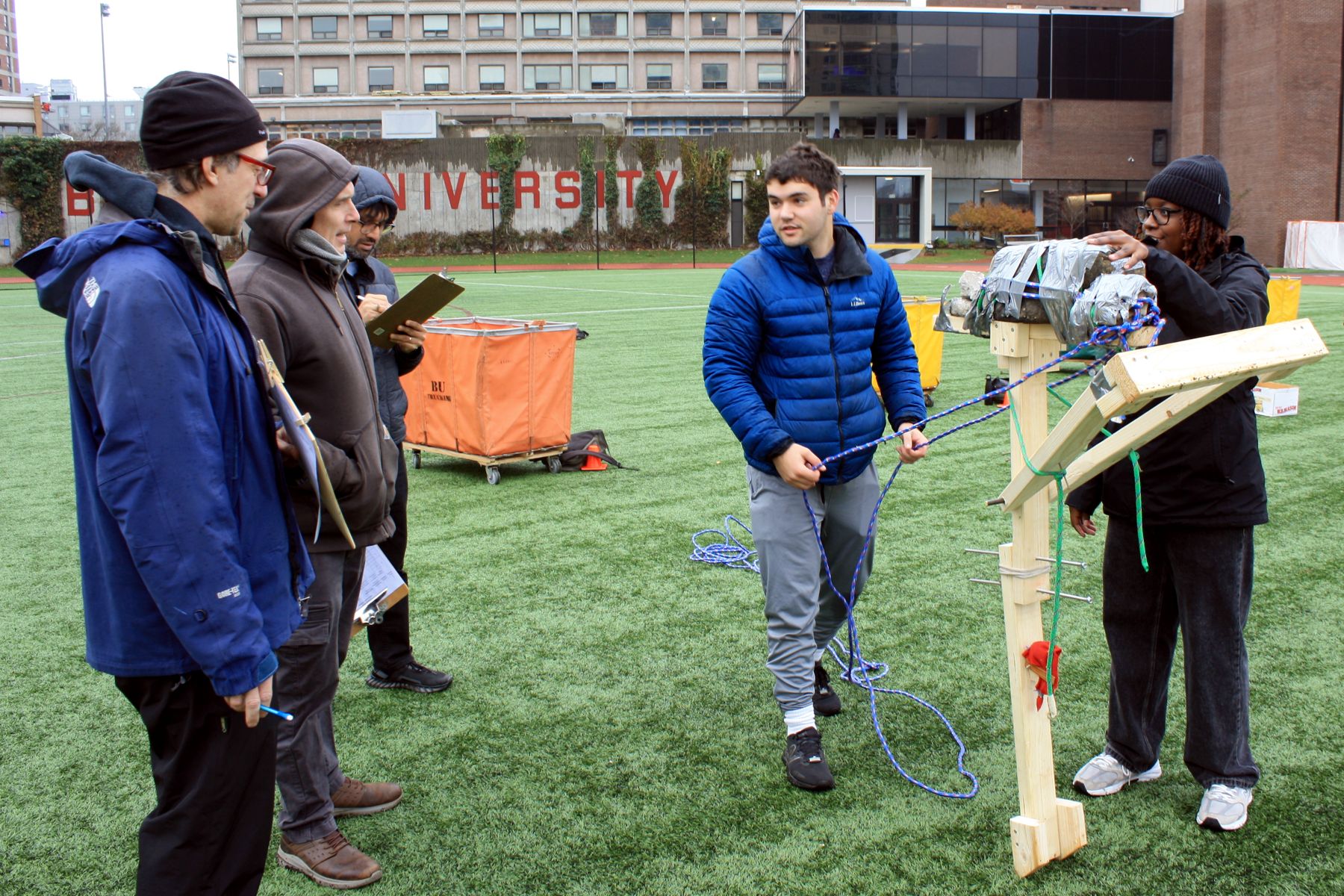 2 students holding their catapult up to show the line of judges on the left how it works